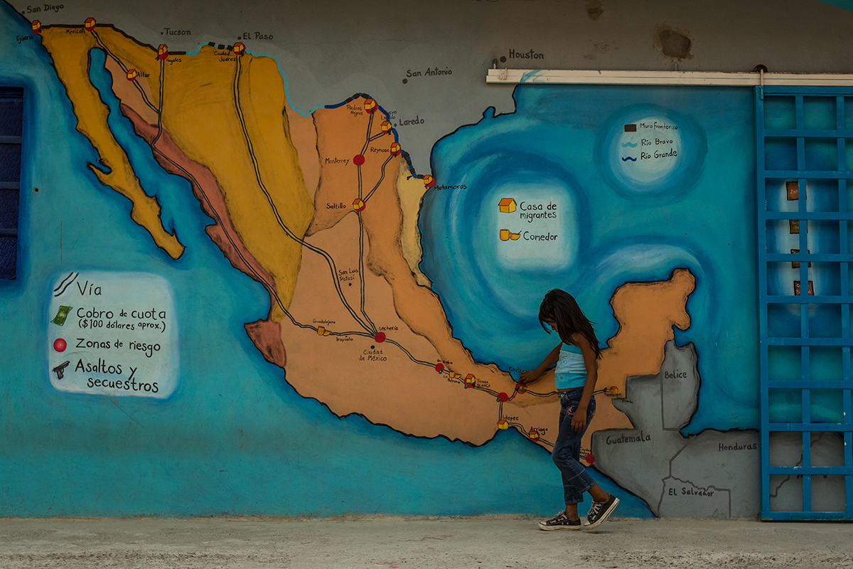 Merlit Melissa Nuñez Rodriguez, 6, who is fleeing with her mother and father to escape gang violence in Olancho, Honduras, in May 2014, looks at a mural of popular routes through Mexico painted on a wall at the migrant shelter Los 72 in Tenosique, Mexico. This shelter provides mats to sleep on, secondhand clothes, meals, basic medical treatment, and help in applying for immigration visas and refugee status for people traveling north. Photo by Meridith Kohut.